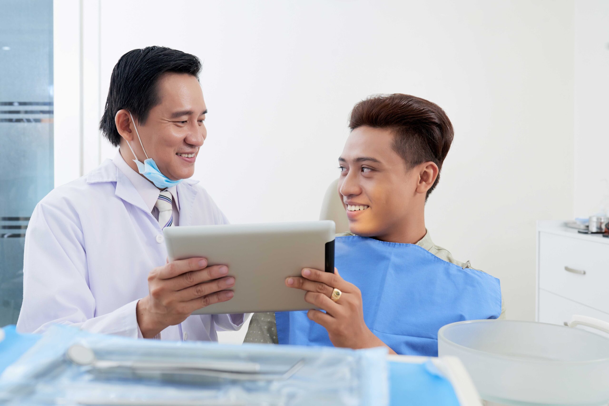 asian-male-dentist-with-tablet-consulting-patient-clinic